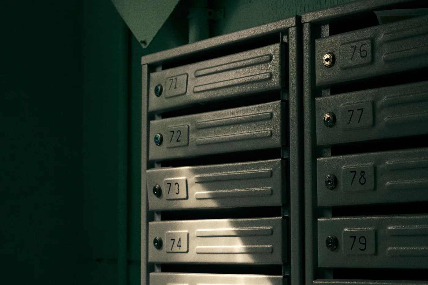 Buzones metálicos numerados del 71 al 79 en el hall de un edificio residencial; fotografía de Ivan Baton en Pexels.