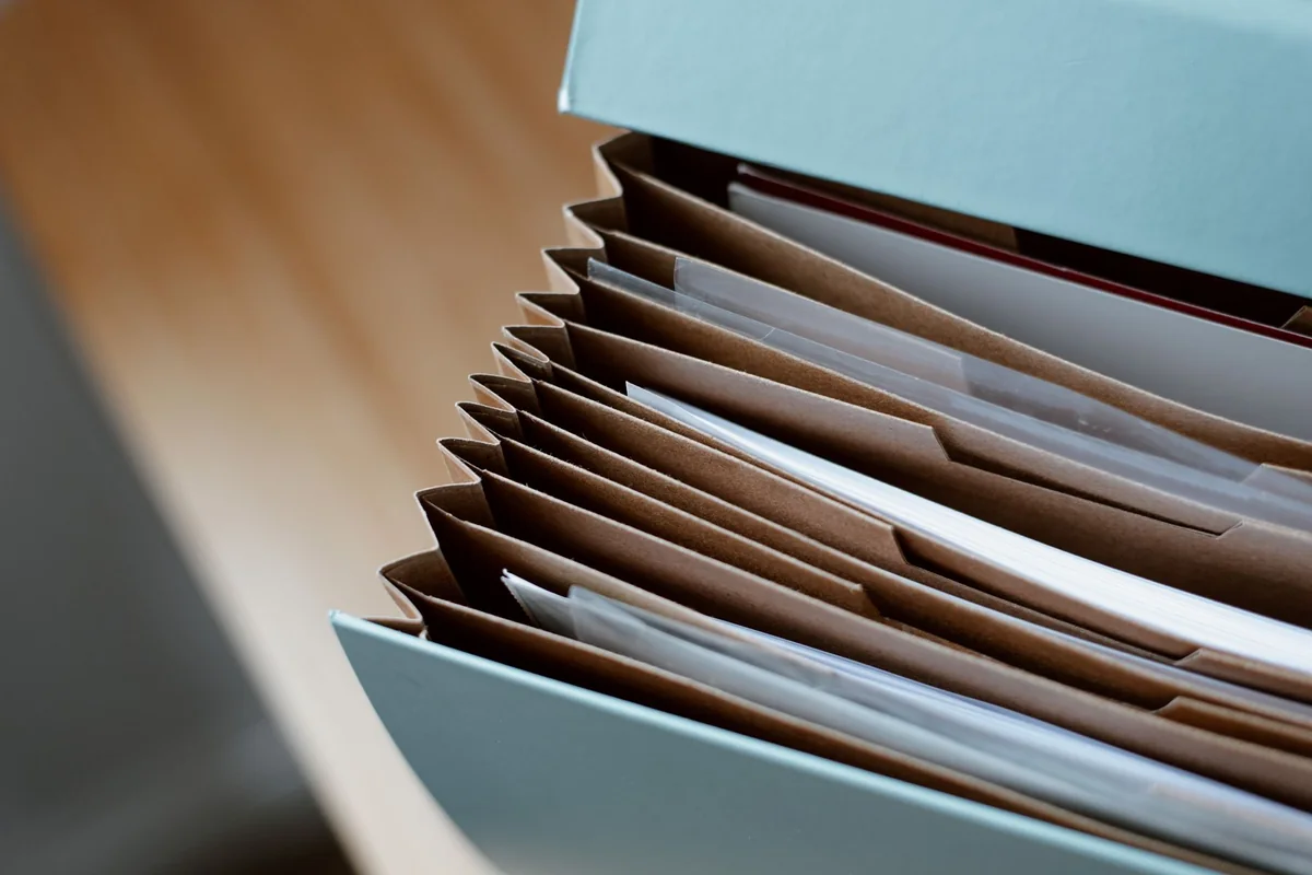 Carpeta de fuelle abierta con separadores de cartón y documentos, sobre un escritorio de madera; fotografía de Anete Lusina en Pexels.